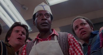 Movie still from “Howard the Duck” (1986), directed by Willard Huyck – A man wearing an apron and a chef's hat stands next to two other people; Close Up shot, Low angle
