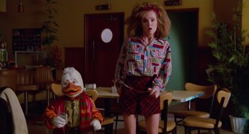 Movie still from “Howard the Duck” (1986), directed by Willard Huyck – A woman in a plaid skirt standing in front of a duck doll; Medium shot, Low angle
