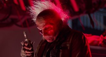 Movie still from “Howard the Duck” (1986), directed by Willard Huyck – An old man with a pink mohawk is looking at his cell phone; Close Up shot, Low angle