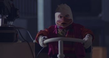 Movie still from “Howard the Duck” (1986), directed by Willard Huyck – A person wearing a duck mask sitting at a steering wheel; Medium shot, Low angle