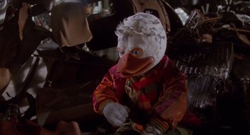 Movie still from “Howard the Duck” (1986), directed by Willard Huyck – A person dressed up as a duck holding a pair of scissors; Medium shot, Low angle