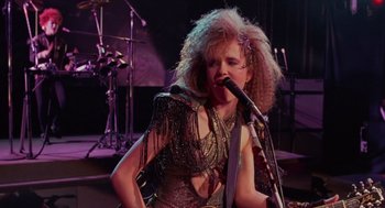 Movie still from “Howard the Duck” (1986), directed by Willard Huyck – A woman in a dress is singing on a stage; Medium shot, Low angle