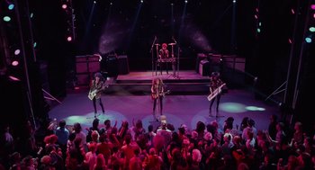 Movie still from “Howard the Duck” (1986), directed by Willard Huyck – A group of people on a stage with guitars; Wide shot, High angle