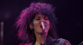 Movie still from “Howard the Duck” (1986), directed by Willard Huyck – A woman in a purple wig singing into a microphone; Close Up shot, Low angle