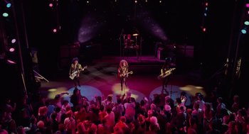 Movie still from “Howard the Duck” (1986), directed by Willard Huyck – A group of people on a stage playing guitar; Wide shot, Overhead angle