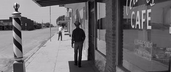 Movie still from “Hud” (1963), directed by Martin Ritt – A black and white photo of a man walking down the sidewalk; Wide shot, Low angle