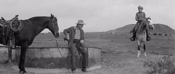 Movie still from “Hud” (1963), directed by Martin Ritt – A man sitting on the side of a wall next to a horse; Wide shot, Low angle