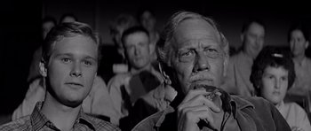 Movie still from “Hud” (1963), directed by Martin Ritt – An older man smoking a cigarette in front of a group of people; Close Up shot, Low angle