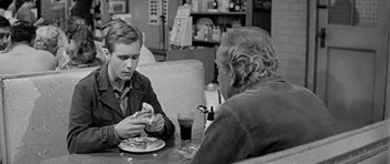 Movie still from “Hud” (1963), directed by Martin Ritt – Two people sitting at a table eating pizza; Medium shot, Over the shoulder angle