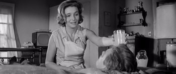 Movie still from “Hud” (1963), directed by Martin Ritt – A woman holding a glass of milk over a woman's head; Medium shot, Low angle