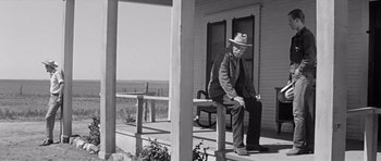 Movie still from “Hud” (1963), directed by Martin Ritt – An older man sitting on a bench on a porch; Wide shot, Low angle