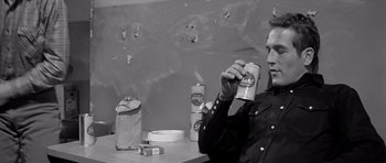 Movie still from “Hud” (1963), directed by Martin Ritt – A man sitting at a table holding a can of beer; Medium shot, Over the shoulder angle
