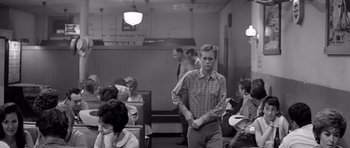 Movie still from “Hud” (1963), directed by Martin Ritt – A man standing in front of a group of people in a room; Medium shot, Over the shoulder angle