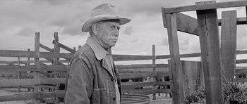 Movie still from “Hud” (1963), directed by Martin Ritt – An older man wearing a hat standing in a fenced in area; Medium shot, Low angle
