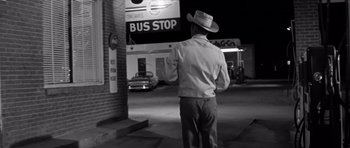 Movie still from “Hud” (1963), directed by Martin Ritt – A black and white photo of a man standing in front of a bus stop at night; Wide shot, Over the shoulder angle