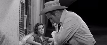 Movie still from “Hud” (1963), directed by Martin Ritt – A man in a cowboy hat talking to a woman in a plaid shirt; Medium shot, Over the shoulder angle