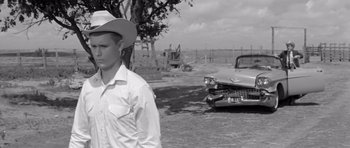Movie still from “Hud” (1963), directed by Martin Ritt – A man wearing a cowboy hat standing in front of an old car; Medium shot, Over the shoulder angle