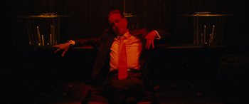 Movie still from “Hustlers” (2019), directed by Lorene Scafaria – A man in a suit and tie sitting on a bench; Medium shot, Low angle