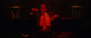 Movie still from “Hustlers” (2019), directed by Lorene Scafaria – A man sitting in a chair holding a drink and wearing a red tie; Medium shot, Low angle