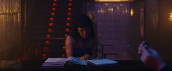 Movie still from “Hustlers” (2019), directed by Lorene Scafaria – A woman sitting at a table writing on a notebook; Medium shot, Over the shoulder angle