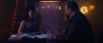 Movie still from “Hustlers” (2019), directed by Lorene Scafaria – A man and a woman sitting at a table with a glass; Medium shot, Over the shoulder angle