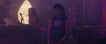 Movie still from “Hustlers” (2019), directed by Lorene Scafaria – A woman standing in a room with a chain around her neck; Medium shot, Over the shoulder angle