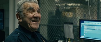 Movie still from “Hustlers” (2019), directed by Lorene Scafaria – An older man in a police uniform smiling for the camera; Close Up shot, Over the shoulder angle