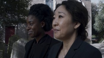 Movie still from “Killing Eve” (2018), created by Phoebe Waller-Bridge – Two women in business suits are smiling for the camera; Close Up shot, Over the shoulder angle