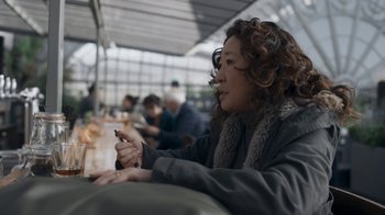 Movie still from “Killing Eve” (2018), created by Phoebe Waller-Bridge – A woman sitting at a table looking at her cell phone; Close Up shot, Over the shoulder angle