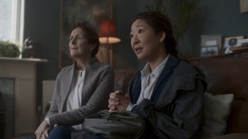 Movie still from “Killing Eve” (2018), created by Phoebe Waller-Bridge – Two women sitting on a couch in front of a lamp; Medium shot, Over the shoulder angle