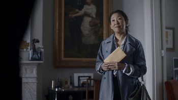 Movie still from “Killing Eve” (2018), created by Phoebe Waller-Bridge – A woman standing in front of a painting holding an envelope; Medium shot, Over the shoulder angle