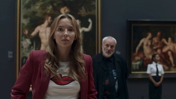 Movie still from “Killing Eve” (2018), created by Phoebe Waller-Bridge – A young woman and an older man standing in front of a painting; Medium shot, Over the shoulder angle