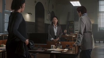 Movie still from “Killing Eve” (2018), created by Phoebe Waller-Bridge – A group of people standing around a table; Wide shot, Over the shoulder angle