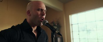 Movie still from “War Dogs” (2016), directed by Todd Phillips – A bald man is singing into a microphone; Close Up shot, Low angle