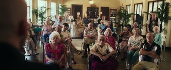Movie still from “War Dogs” (2016), directed by Todd Phillips – A group of elderly people sitting in a living room; Wide shot, High angle