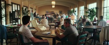 Movie still from “War Dogs” (2016), directed by Todd Phillips – A man sitting at a table in front of an open book; Wide shot, Over the shoulder angle