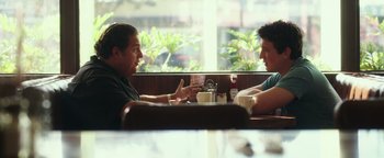 Movie still from “War Dogs” (2016), directed by Todd Phillips – Two men are sitting at a table in a restaurant; Medium shot, Over the shoulder angle