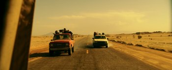 Movie still from “War Dogs” (2016), directed by Todd Phillips – Two cars driving down a dirt road in the middle of the desert; Wide shot, Low angle