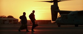 Movie still from “War Dogs” (2016), directed by Todd Phillips – Two people walking on a runway near a helicopter; Wide shot, Low angle
