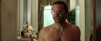 Movie still from “War Dogs” (2016), directed by Todd Phillips – A shirtless man wearing glasses and a necklace in front of a window; Close Up shot, Over the shoulder angle