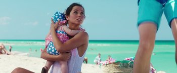 Movie still from “War Dogs” (2016), directed by Todd Phillips – A woman holding a baby on the beach near the ocean; Medium shot, Over the shoulder angle