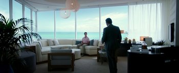Movie still from “War Dogs” (2016), directed by Todd Phillips – A man in a suit and tie standing in front of another man in a suit and tie in front of an ocean view window; Wide shot, Over the shoulder angle