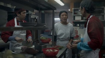 Movie still from “Killing Eve” (2018), created by Phoebe Waller-Bridge – A group of people standing around a kitchen preparing food; Medium shot, Over the shoulder angle