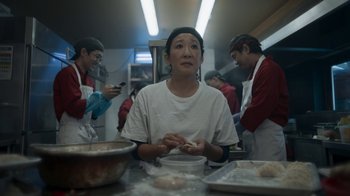 Movie still from “Killing Eve” (2018), created by Phoebe Waller-Bridge – A woman sitting at a table in front of a pan of food; Close Up shot, Over the shoulder angle