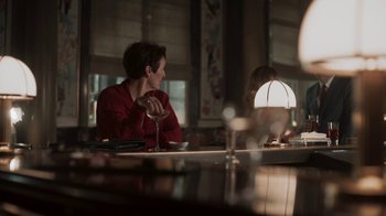 Movie still from “Killing Eve” (2018), created by Phoebe Waller-Bridge – A woman sitting at a table in a restaurant; Medium shot, Over the shoulder angle
