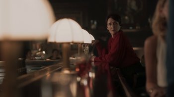 Movie still from “Killing Eve” (2018), created by Phoebe Waller-Bridge – A woman sitting at a table in front of a table lamp; Medium shot, Over the shoulder angle
