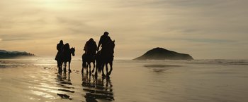 Movie still from “War for the Planet of the Apes” (2017), directed by Matt Reeves – A group of people riding horses on top of a sandy beach; Extreme Wide shot, Low angle