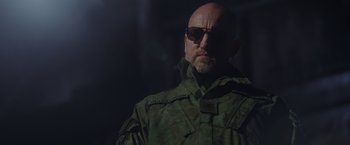Movie still from “War for the Planet of the Apes” (2017), directed by Matt Reeves – A bald man in a green jacket and sunglasses; Close Up shot, Low angle