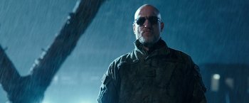 Movie still from “War for the Planet of the Apes” (2017), directed by Matt Reeves – A bald man wearing sunglasses in the rain; Close Up shot, Low angle