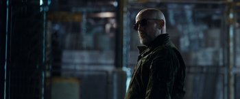 Movie still from “War for the Planet of the Apes” (2017), directed by Matt Reeves – A man with a beard wearing sunglasses standing in a dark room; Medium shot, Low angle